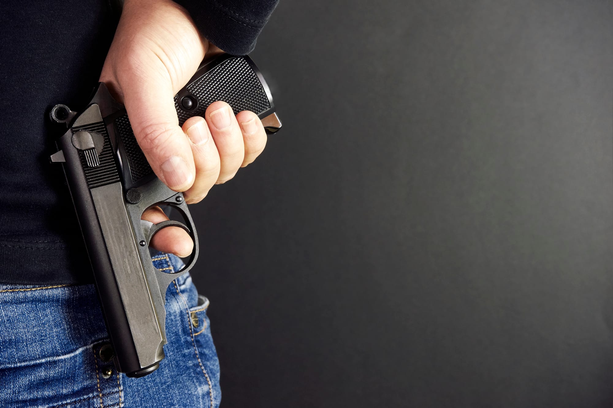 Image of a man discreetly concealing a firearm behind his back, illustrating the concept of felony possession of a firearm